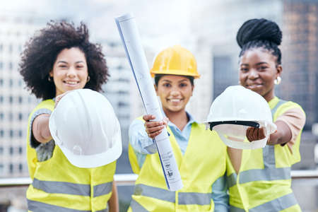 The site managers are here to do their inspection. Portrait of a group of confident young businesswomen holding blueprints and hardhats while working at a construction site.の写真素材