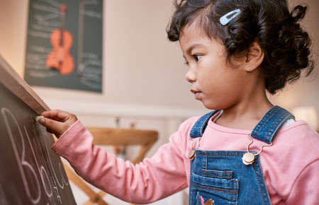 Focused on learning her alphabet. a little girl writing on a blackboard at home.の写真素材