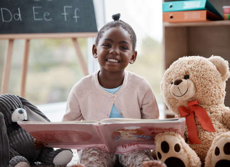 Come sit with me for story time. an adorable little girl reading a book while sitting at home.の写真素材