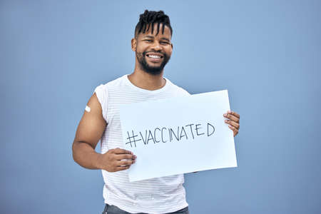 The vaccine is the right choice. a handsome young man standing alone in the studio and holding a poster after getting his Covid vaccine.の写真素材
