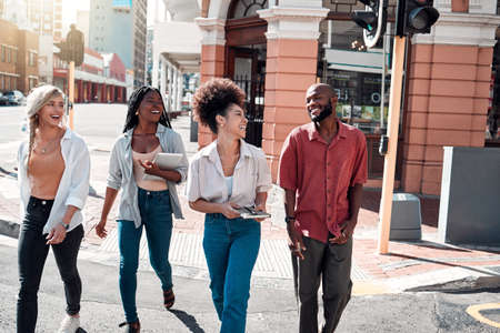 Casual, diverse students walking in the city and chatting or having fun together in town during a university campus break. Cheerful, happy group of friends enjoying an outdoor meeting or hanging out.の写真素材