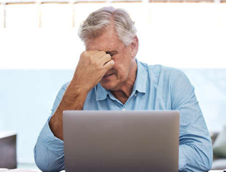 This is so frustrating. a mature man sitting alone and feeling stressed while using his laptop to...