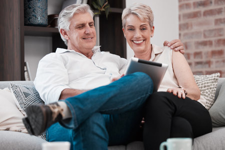 Wealth is a crown only seen the impoverished. a mature couple using a digital tablet at home on the sofa together.の写真素材