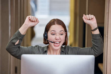 Yay You found it. a young call centre agent sitting alone in the office and celebrating a success wile using her computer.の写真素材