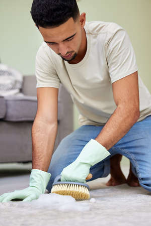 Scrubbing all the dirt away. a young man scrubbing the floor at home.の写真素材