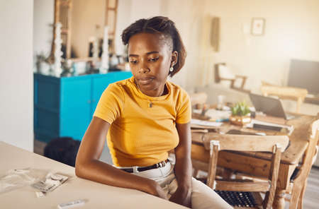 A woman waiting for the results from the kit at home. Young casual African woman looking at her virus or infection diagnosis from self testing equipment in her houseの写真素材