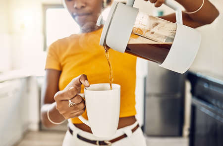 Hands of woman pouring coffee into a mug, standing inside a kitchen at home. French press with homemade, fresh, and delicious warm drink to start the morning or day with a brewed caffeine beverageの写真素材