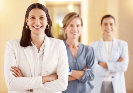 Success is best when its shared. Portrait of a young businesswoman standing with her arms crossed in an office with her colleagues in the background.の写真素材