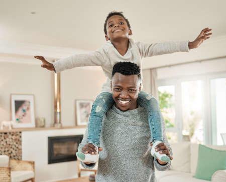 Lets go dad. Cropped portrait of a handsome young man carrying his son on his shoulders in the living room at home.の写真素材