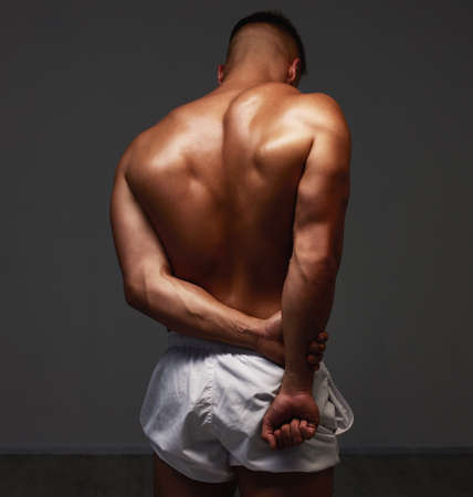 Flexing his muscles. Rearview shot of an unrecognizable and athletic young man posing shirtless in...
