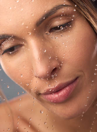 Rejuvenate your body and senses with a relaxing shower. Studio shot of a beautiful young woman taking a shower against a grey background.の写真素材