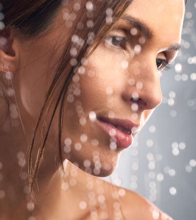 Good hygiene is the foundation of vibrant skin. Studio shot of a beautiful young woman taking a shower against a grey background.の写真素材