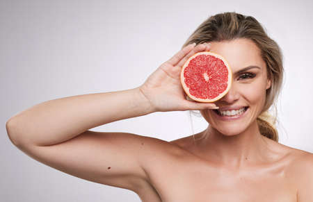 Beauty itself is but the sensible image of the Infinite. Studio shot of a beautiful young woman posing with a grape fruit against a grey background.の写真素材