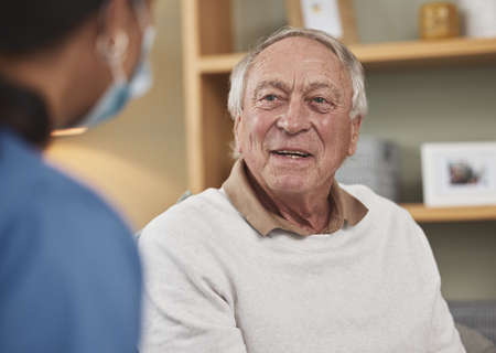 A happy and cared for patient. an elderly man having a checkup with an unrecognizable nurse at home.