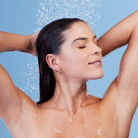 Wash your troubles away. Studio shot of a young woman taking a shower against a blue background.