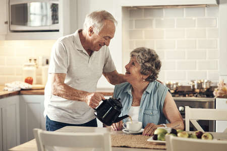 Would you like some tea. a senior couple having breakfast together at home.の写真素材