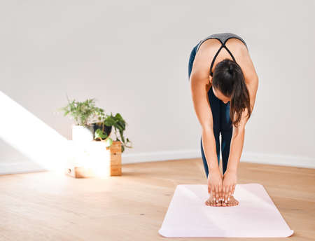 Reach for your toes. a young woman practicing yoga at home.