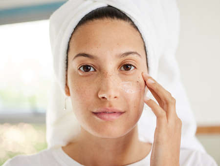 If you have a good moisturiser then you have everything you need. a beautiful young woman applying moisturiser to her face.の写真素材