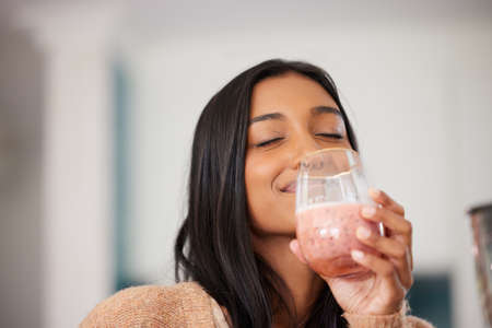 So much nutrients packed into one delicious drink. a young woman drinking a healthy smoothie at home.の写真素材