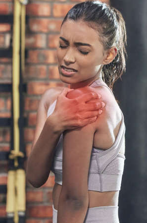 This is going to set me back in my workout. a sporty young woman experiencing shoulder pain in a gym.の写真素材