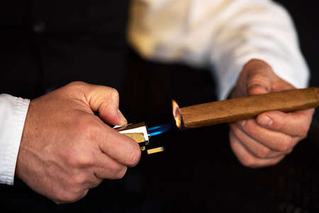 Treat yourself to the finer things in life. an unrecognizable man lighting a cigar with a lighter.