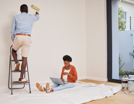 Taking the weight of my feet while he paints. Full length shot of a young couple redecorating a room at home with fresh paint.の写真素材