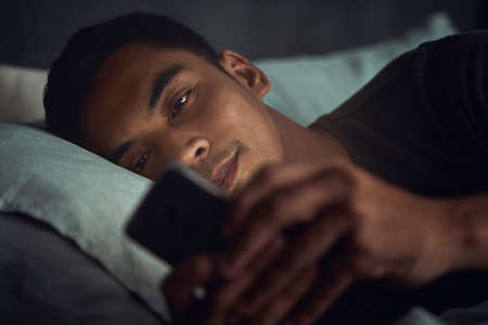 When social media is sweeter than your dreams. a young man lying in bed and using a smartphone at...