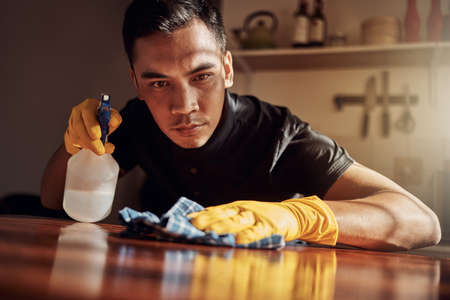 Im on the sanitising squad. a young man disinfecting a kitchen counter at home.の写真素材
