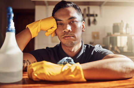 I should have called a cleaning service. Portrait of a young man looking unhappy after cleaning the kitchen at home.の写真素材