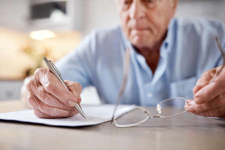Admin knows no age. an elderly man filling in forms at the kitchen table at home.の写真素材
