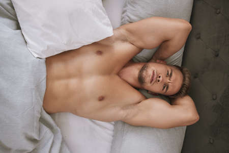 This morning just got sexy. High angle portrait of a handsome and muscular young man lying in his bed at home.の写真素材