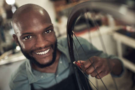 We provide quality service here. a handsome young man standing alone in his shop and repairing a bicycle wheel.の写真素材