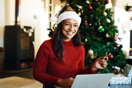 Christmas shopping just got so much easier. a happy young woman using a laptop and credit card during Christmas at home.の写真素材
