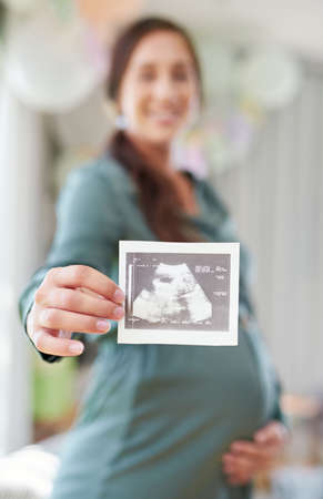 Ive been staring at you for ages. a young mother to be holding an ultrasound of her unborn child.の写真素材
