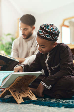 You can only provide the right conditions for learning. a young muslim man and his son reading in the lounge at home.の写真素材