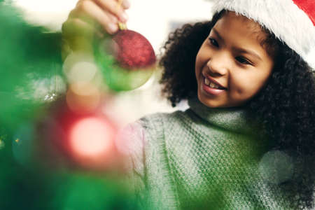 Santas little helper took the day off so here I am. a cute little girl decorating a Christmas tree at home.の写真素材