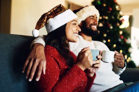 Hot chocolate and happy Christmas memories. a happy young couple relaxing on the sofa and having warm drinks during Christmas at home.の写真素材