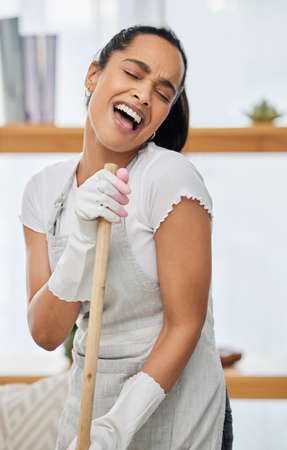 Happiness is a clean home. an attractive young woman standing and singing while using a broom to sweep her home.の写真素材