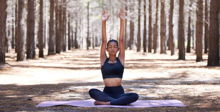 Releasing all that no longer serves me. an attractive young woman sitting alone on a yoga mat outdoors and meditating.の写真素材