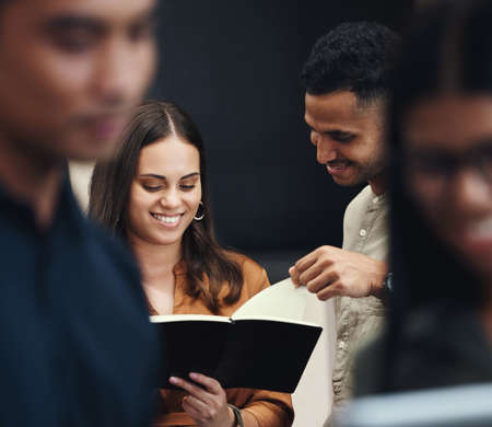 Lets see what youve got there. two young businesspeople looking over a notebook near the back of...
