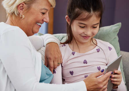 Lets test your intelligence now, gran. an adorable little girl using a digital tablet while sitting...