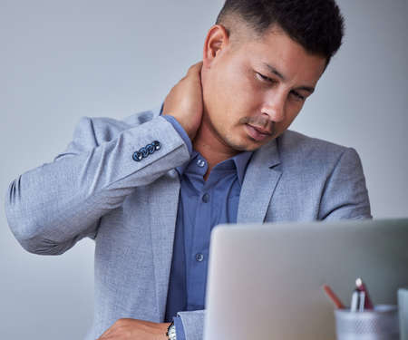 Someone get me a massage. a young businessman experiencing neck pain at work.の写真素材