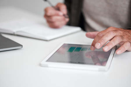 Wireless is the way to go. High angle shot of an unrecognizable businessman using a tablet while sitting at his desk in the office.の写真素材
