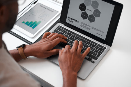 Putting his hands to work. High angle shot of an unrecognizable businessman using a laptop while sitting at his desk in the office.の写真素材