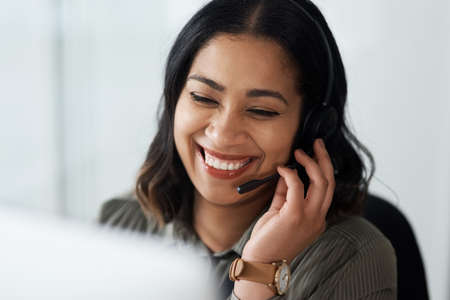 Fast and friendly, thats what people say about our services. a young businesswoman wearing a headset while working in a call centre.の写真素材