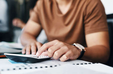 Calculating the minutes until the end of the day. an unrecognizable businessman using a calculator in an office.の写真素材