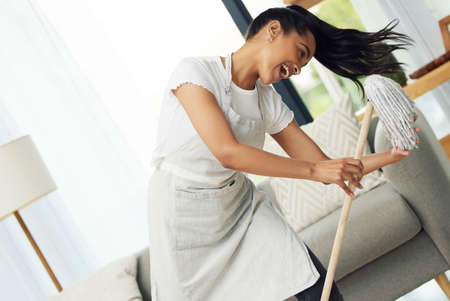 Dont let chores, get you down, have fun with it. a cheerful woman dancing with a mop at home.の写真素材