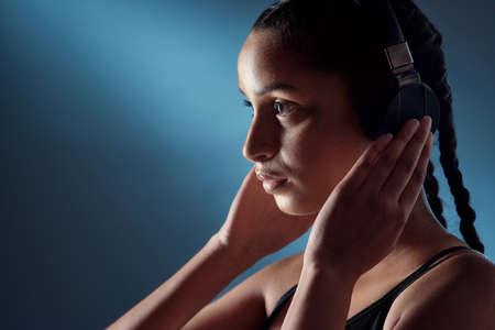 Change your mindset and everything else automatically does too. Studio shot of a sporty young woman listening to music against a blue background.の写真素材