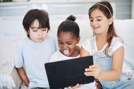 We love making funny faces. a group of little children using a digital tablet at home.