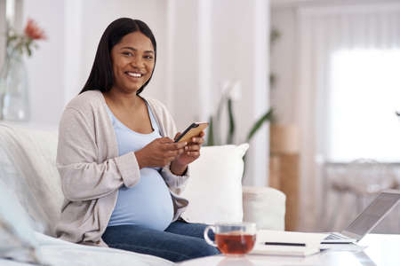 Everyone believes that Im resting in bed since my leave started. a pregnant woman using her cellphone while sitting at home.の写真素材